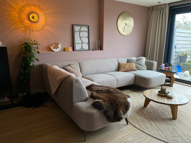 Binnenkijker met lichte hoekbank, ronde salontafel en warme aardetinten